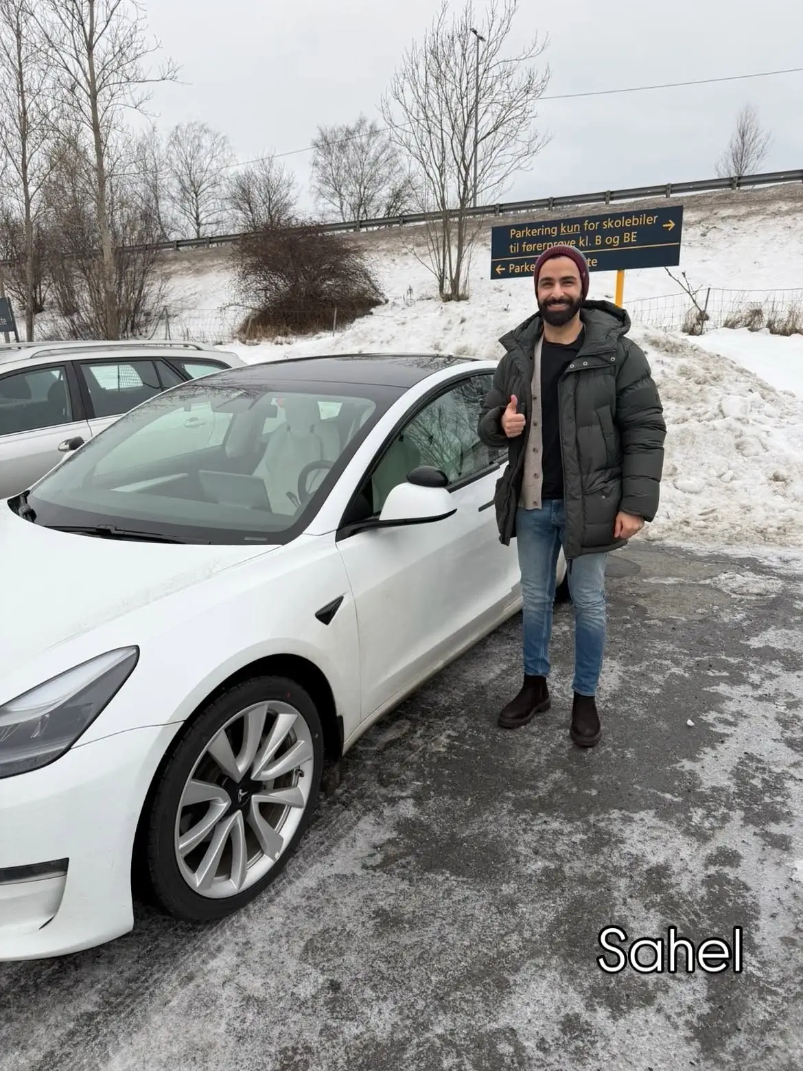 Sahel smiler ved skolens hvite Tesla etter bestått førerprøve