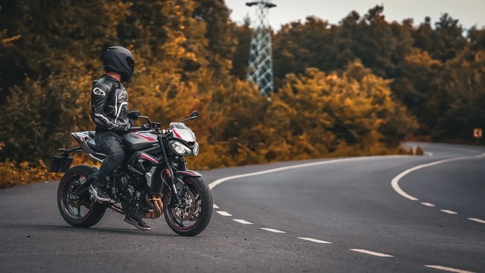 Motorsyklist på en Triumph i en tom sving omgitt av høstskog