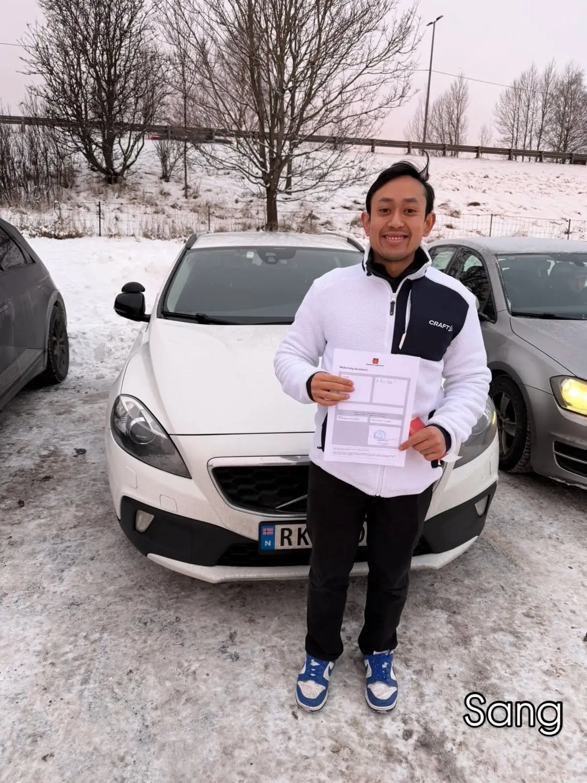 Elev holder opp førerkortbeviset foran skolebilen